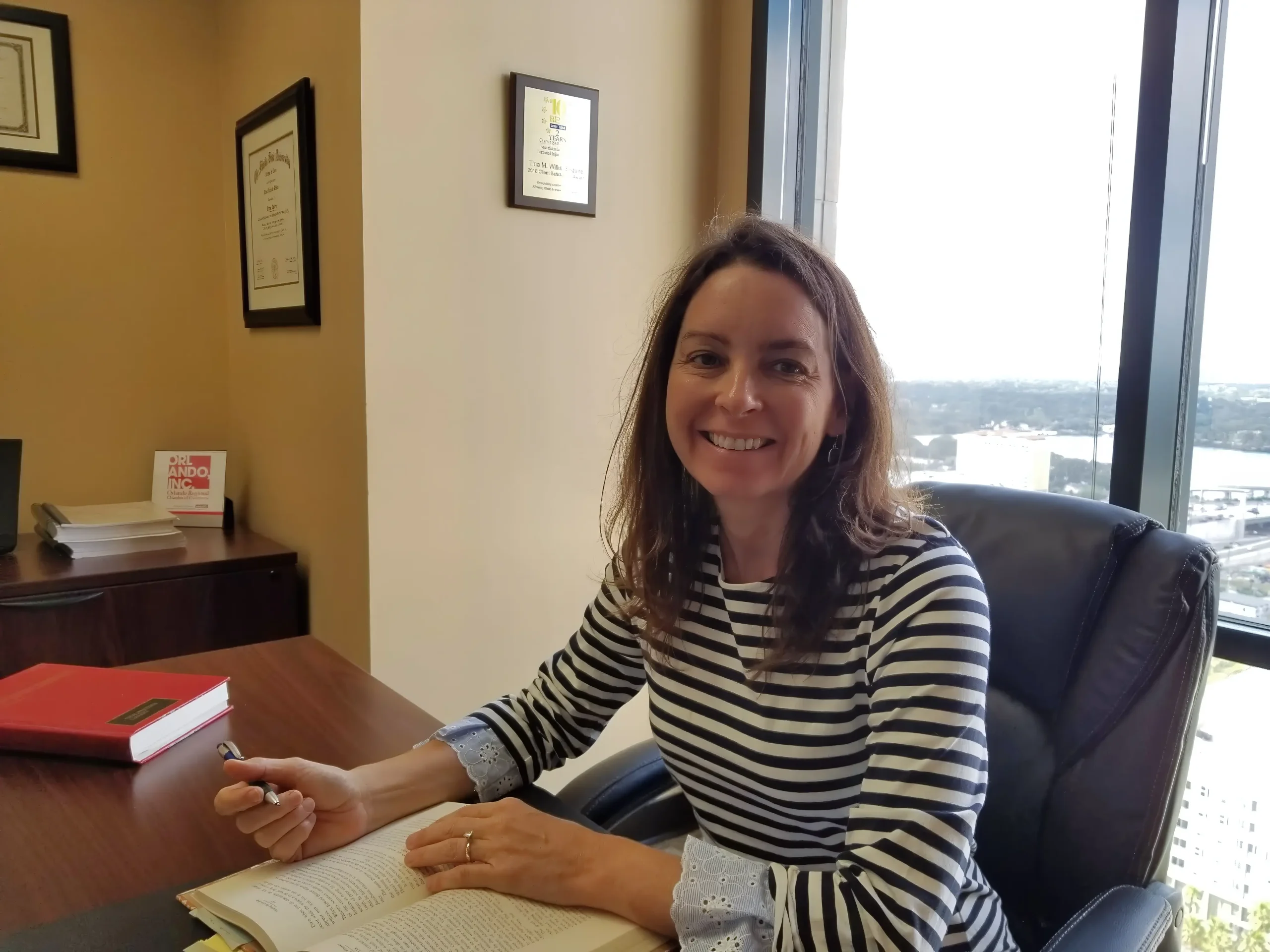 Orlando personal injury attorney Tina Willis at desk in downtown Orlando office with awards and credentials